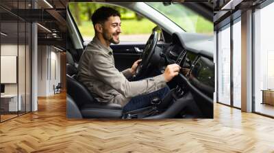 Young man sitting on car turning on radio at street Wall mural